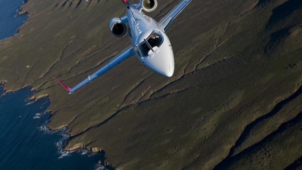 Ein Privatjet fliegt über eine zerklüftete Küstenlandschaft.