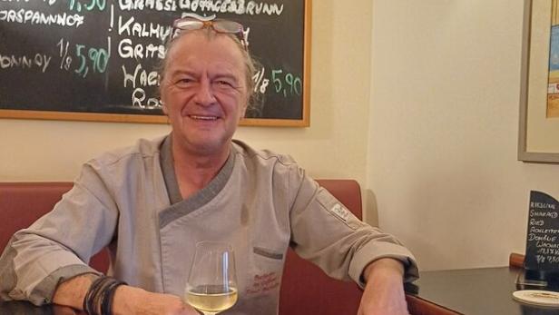 Wirt Franz Buchecker sitzt unter einer Tafel, auf der die Weinkarte zu sehen ist.