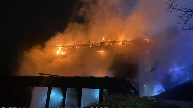 Eine Nachaufnahme von orangenen Flammen, die das Dach eines Hauses einnehmen.