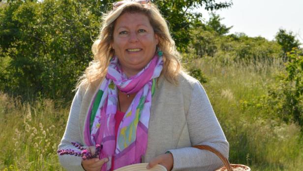 Eunike Grahofer steht mit einem braunen geflochtenen Korb auf einer Wiese und hält eine Schüssel mit Pflanzen.
