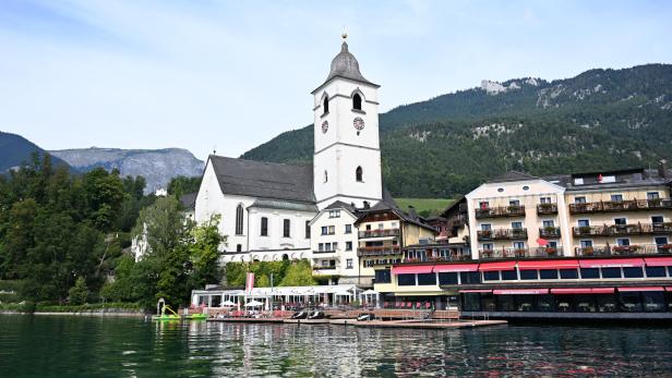++ THEMENBILD ++ WOLFGANGSEE-JUBILÄUMSJAHR 2024 - 1.100 JAHRE HEILIGER WOLFGANG / WALLFAHRTSKIRCHE ST. WOLFGANG Eine weiße Kirche mit Turm steht am Ufer eines Sees, umgeben von Hotels und bewaldeten Bergen im Hintergrund.