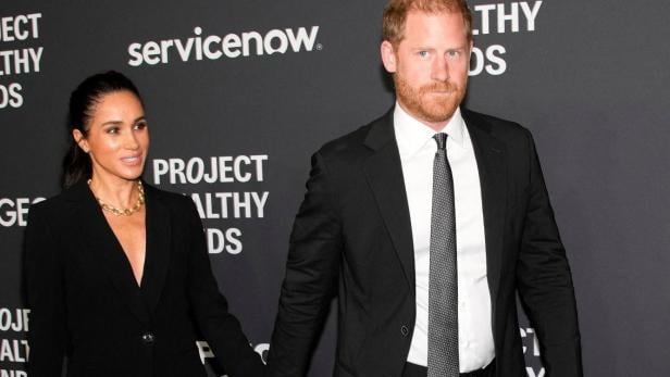Meghan und Prinz Harry Hand in Hand vor dunklem Hintergrund mit Schriftzügen.