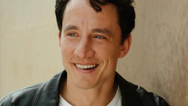 Ein lachender jüngerer Mann mit dunklem Haar.