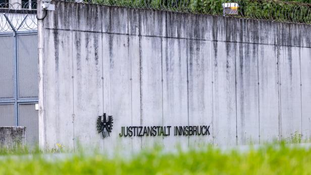 Eine graue Betonmauer mit Stacheldraht und der Aufschrift "Justizanstalt Innsbruck" ist zu sehen.