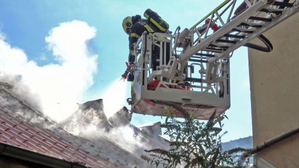 Ein Feuerwehrmann steht im Korb eines Hubrettungsfahrzeugs und löscht Flammen auf einem Dach.
