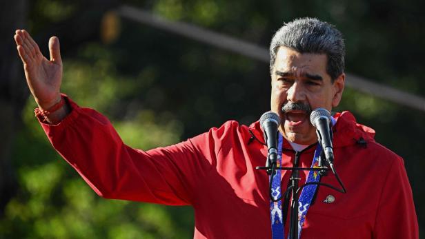 Maduro in roter Jacke gestikuliert vor zwei Mikrofonen.