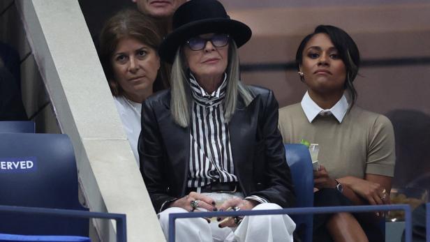Diane Keaton sitzt mit Hut und gestreifter Bluse auf einem reservierten Platz.