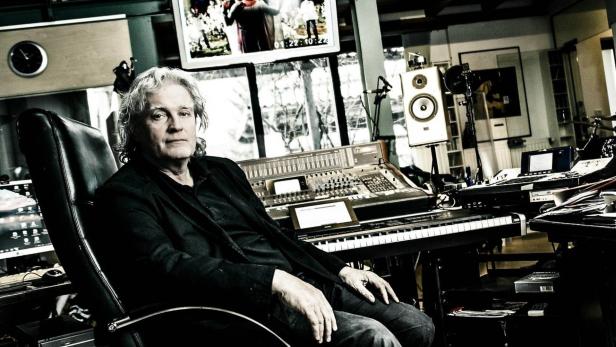 Ein Mann mit grauen Haaren sitzt in einem Tonstudio vor Mischpult, Keyboard und Lautsprechern.