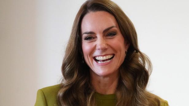 Lachende Prinzessin Kate mit gewellten Haaren trägt ein grünes Oberteil.