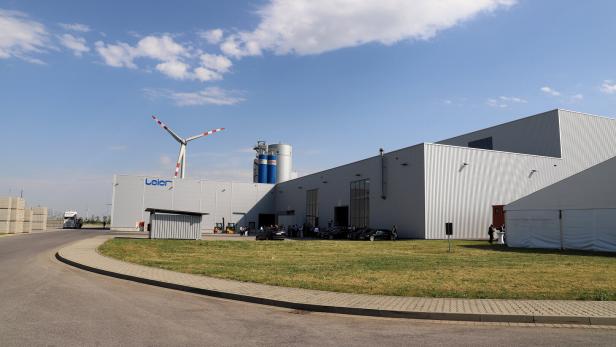 Ein Leier-Werk mit Windrad und Silos unter blauem Himmel mit Wolken.