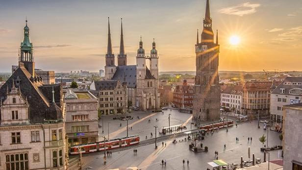 Sonnenuntergang über einem Stadtplatz mit markanten Türmen im Hintergrund.