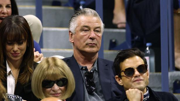 Alec Baldwin und Anna Wintour sitzen mit anderen Zuschauern auf einer Tribüne.