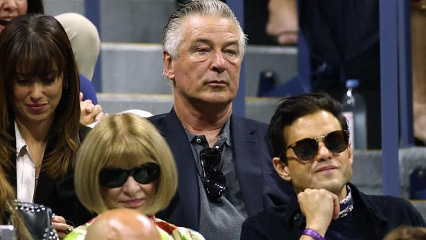 Alec Baldwin und Anna Wintour sitzen mit anderen Zuschauern auf einer Tribüne.