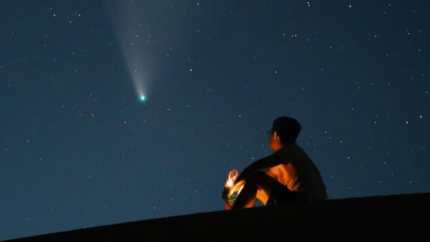 Sternenhimmel Mann sitzt nachts auf einem Hügel und blickt in den Sternenhimmel