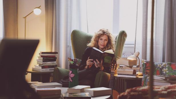 Lotte de Beer beim Lesen in einem Sessel - vor ihr türmen sich Bücher.