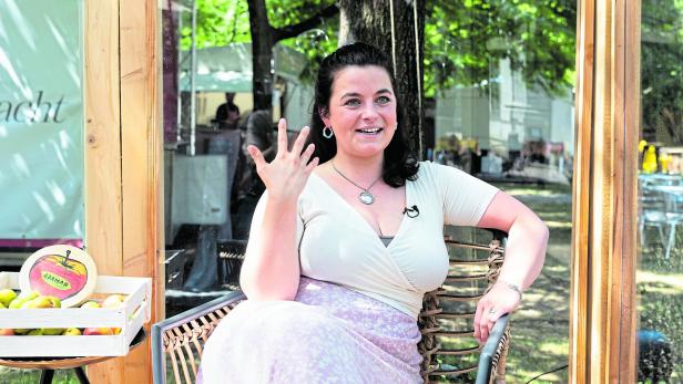 Talk mit Schauspielerin Ronja Forcher Eine Frau sitzt lächelnd auf einem Stuhl im Freien, gestikuliert mit der Hand und trägt ein Mikrofon am Oberteil.