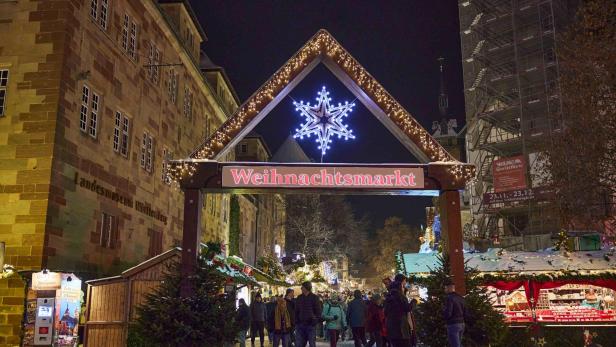 Eingang zum Weihnachtsmarkt mit beleuchtetem Schneeflockensymbol und Schriftzug 'Weihnachtsmarkt', Menschen und Stände bei Nacht.