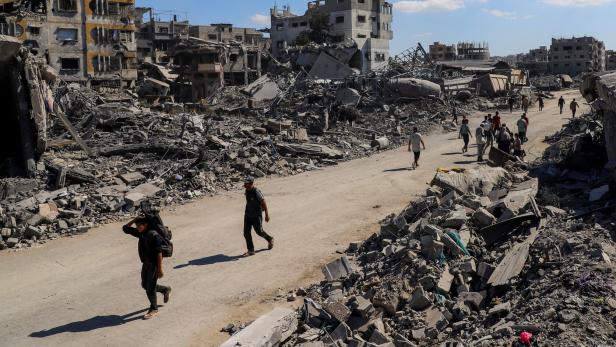 Palestinians walk past the rubble of destroyed buildings, amid a ceasefire between Israel and Hamas, in Gaza City