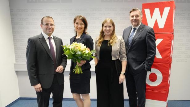 Vier Personen posieren vor einem roten WKO-Logo, eine Frau hält einen Blumenstrauß.
