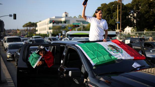 Protestors gather around the Los Angeles Federal Building after multiple detentions by ICE, Los Angeles Eine Person steht durch das Schiebedach eines Autos mit einer mexikanischen Flagge, während eine andere Person aus dem Fenster schaut.