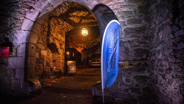 Ein gemauerter Steindurchgang, der Teil einer alten Burg oder eines alten Schlosses ist. Davor ist eine blaue Fahne mit "Wachau in Echtzeit" montiert.