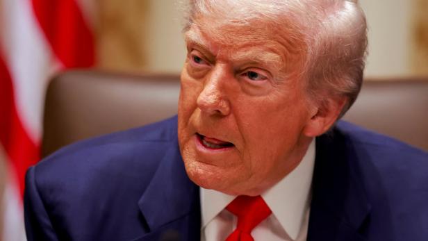 Ein älterer Mann mit blonden Haaren trägt einen blauen Anzug, ein weißes Hemd und eine rote Krawatte.