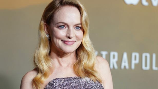 Heather Graham mit langen blonden Haaren trägt ein glitzerndes, schulterfreies Kleid und lächelt.