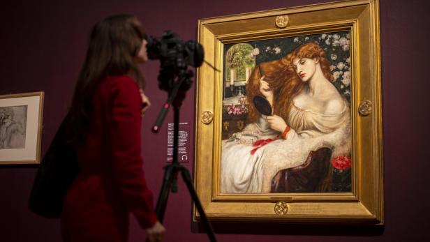 Eine Person fotografiert ein gerahmtes Gemälde einer rot haarigen Frau in einer Galerie.
