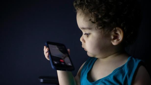 Kleiner Junge im blauen Tanktop hält ein schwarzes Handy in Händen