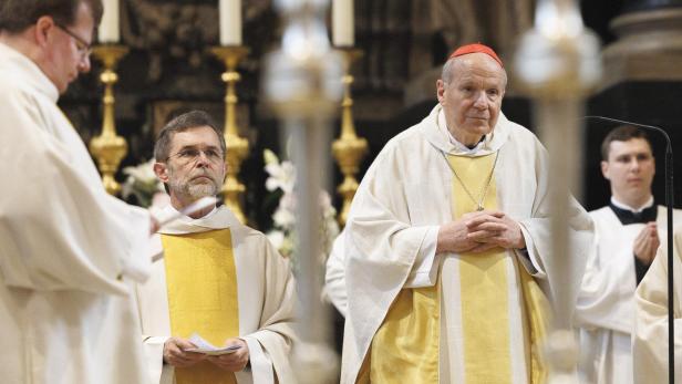 Josef Grünwidl und Christoph Schönborn. in weißen und gelben liturgischen Gewändern stehen in einer Kirche vor goldenen Kerzenhaltern.