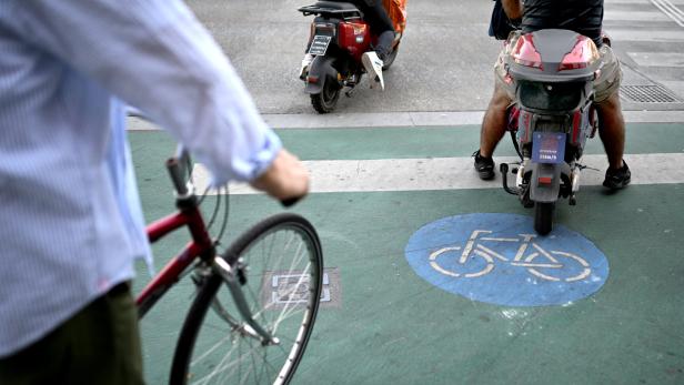 Ein Radfahrer und zwei Roller sind auf einem Radweg zu sehen.