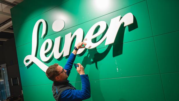 Ein Mann befestigt weiße Buchstaben an einer großen grünen Wand mit dem Schriftzug „Leiner“.