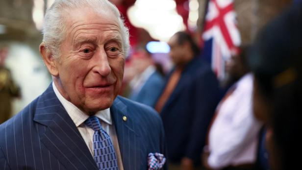 König Charles III. im Nadelstreifenanzug mit blau gemusterter Krawatte lächelt in die Kamera.