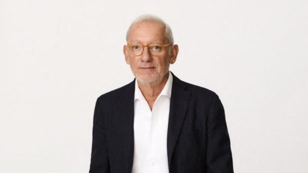 Isak Andic mit Brille, Jeans und Sakko sitzt vor einem hellen Hintergrund.