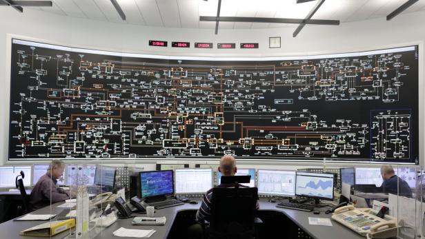 Ist das Stromnetz gut ausgelastet und der Strom günstig, ist der ideale Zeitpunkt, um industrielle Anlagen damit zu betreiben. Stromnetz-Kontrollraum mit riesigem Display und Mitarbeitern vor Computern.