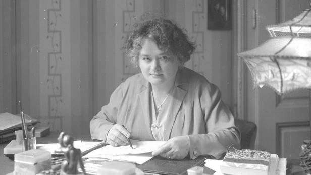 Popp, Adelheid Eine Frau mit lockigem Haar, Adelheid Popp, sitzt an einem Schreibtisch und schreibt mit einem Stift auf Papier.