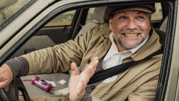 Uhudler Verschwörung - Ein Stinatz Krimi Man sitzt am Steuer eines Autos und lacht