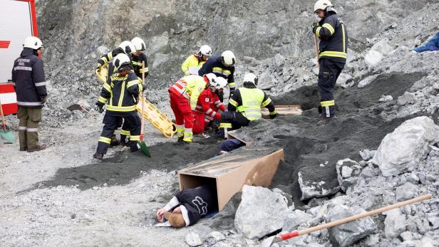 46-219534448 Einsatzkräfte bergen eine Person aus einem Karton vor einer Felswand.