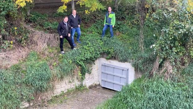 Drei Männer vor neuem Hochwasserschutz bei einem Bach