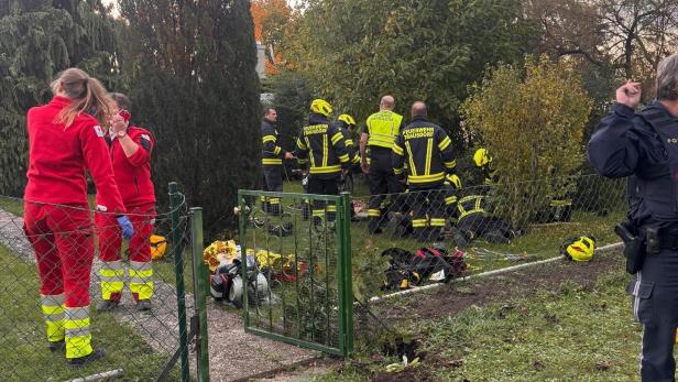 Mehrere Feuerwehrleute und Rettungskräfte arbeiten in einem Garten hinter einem offenen Gartentor, Ausrüstung liegt auf dem Boden.