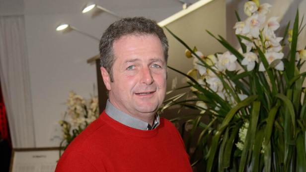 Norbert Rier Norbert Rier mit rotem Pullover steht neben einer hohen Pflanze mit weißen Blüten.