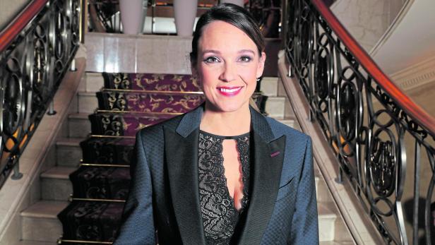 Carolin Kebekus Carolin Kebekus mit Blazer und Spitze steht vor einer Treppe mit Teppich.