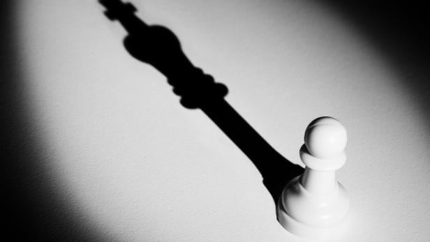 Chess pawn standing in a spotlight that make a shadow of king with darkness actistic conversion