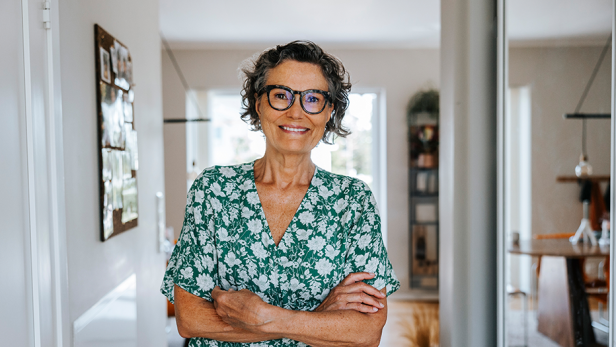 Eine Frau mit Brille steht in einem Flur und lächelt in die Kamera.