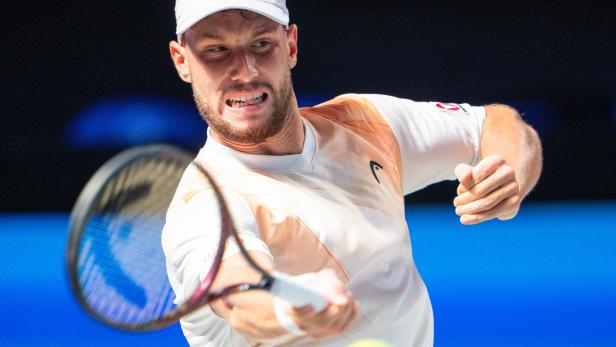 Ein Tennisspieler schlägt mit konzentriertem Gesichtsausdruck einen gelben Ball mit dem Schläger.