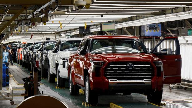FILE PHOTO: Automaker group warns Nexperia chip supply issue could quickly disrupt US production Mehrere neue Pick-up-Trucks stehen hintereinander in einer hell beleuchteten Autofabrik, während Arbeiter sie überprüfen.
