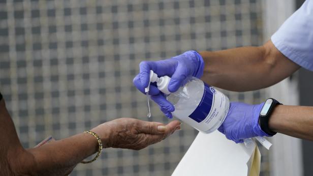 Eine Person mit Handschuhen gibt Desinfektionsmittel auf die Hand einer anderen Person.