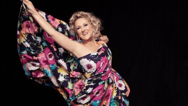 Eine Frau weht mit ihrem Kleid mit Blumenaufdruck und lächelt in die Kamera.