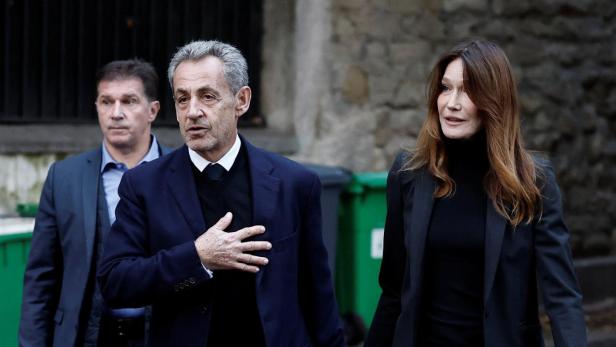 Nicolas Sarkozy und Carla Bruni gehen Händchen haltend, begleitet von einem Mann.