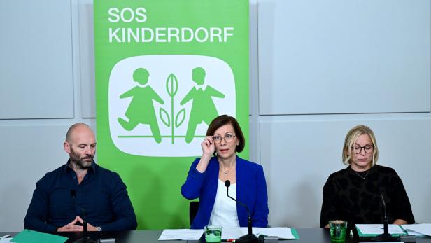 PG SOS-KINDERDORF: RUDISCH / SCHLACK / CERNY Drei Personen sitzen vor einem SOS-Kinderdorf Banner an einem Tisch.